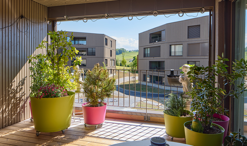 Loggia mit Pflanzenkübeln und Holzrost, Blick in den autofreien Innenhof der Siedlung.