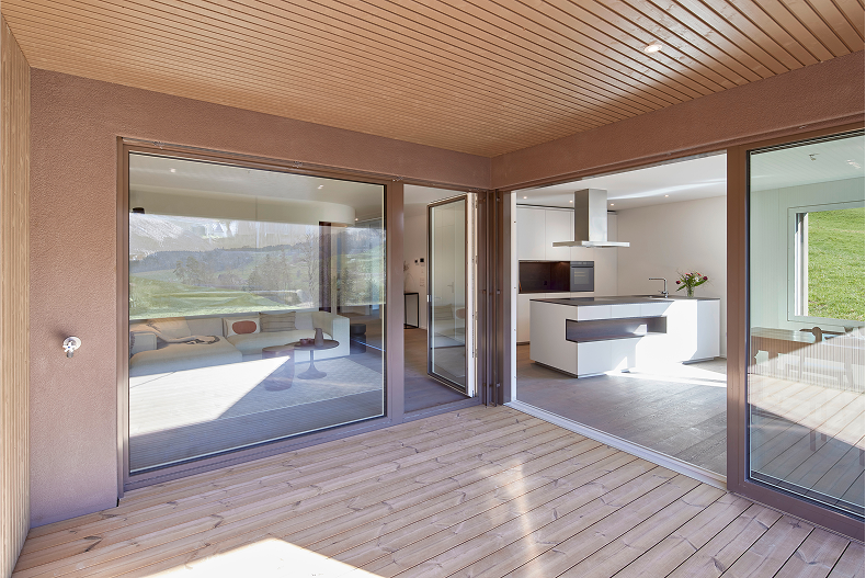 Grosszügige, überdachte Terrasse mit Holzdeck; raumhohe Schiebetüren zu Wohn- und Küchenbereich.